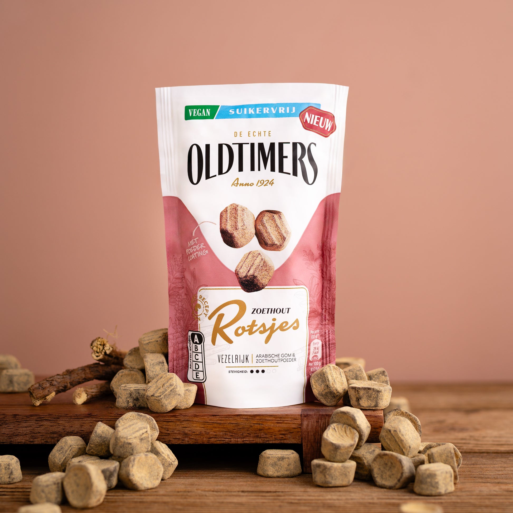 Oldtimers Zoethout Rotsjes suikervrije vegan snoepjes in een staande verpakking, omringd door zoethoutblokjes op een houten ondergrond.