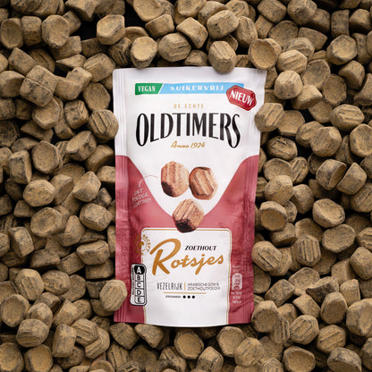 Oldtimers Zoethout Rotsjes suikervrije vegan snoepjes in een staande verpakking, omringd door zoethoutblokjes op een houten ondergrond.