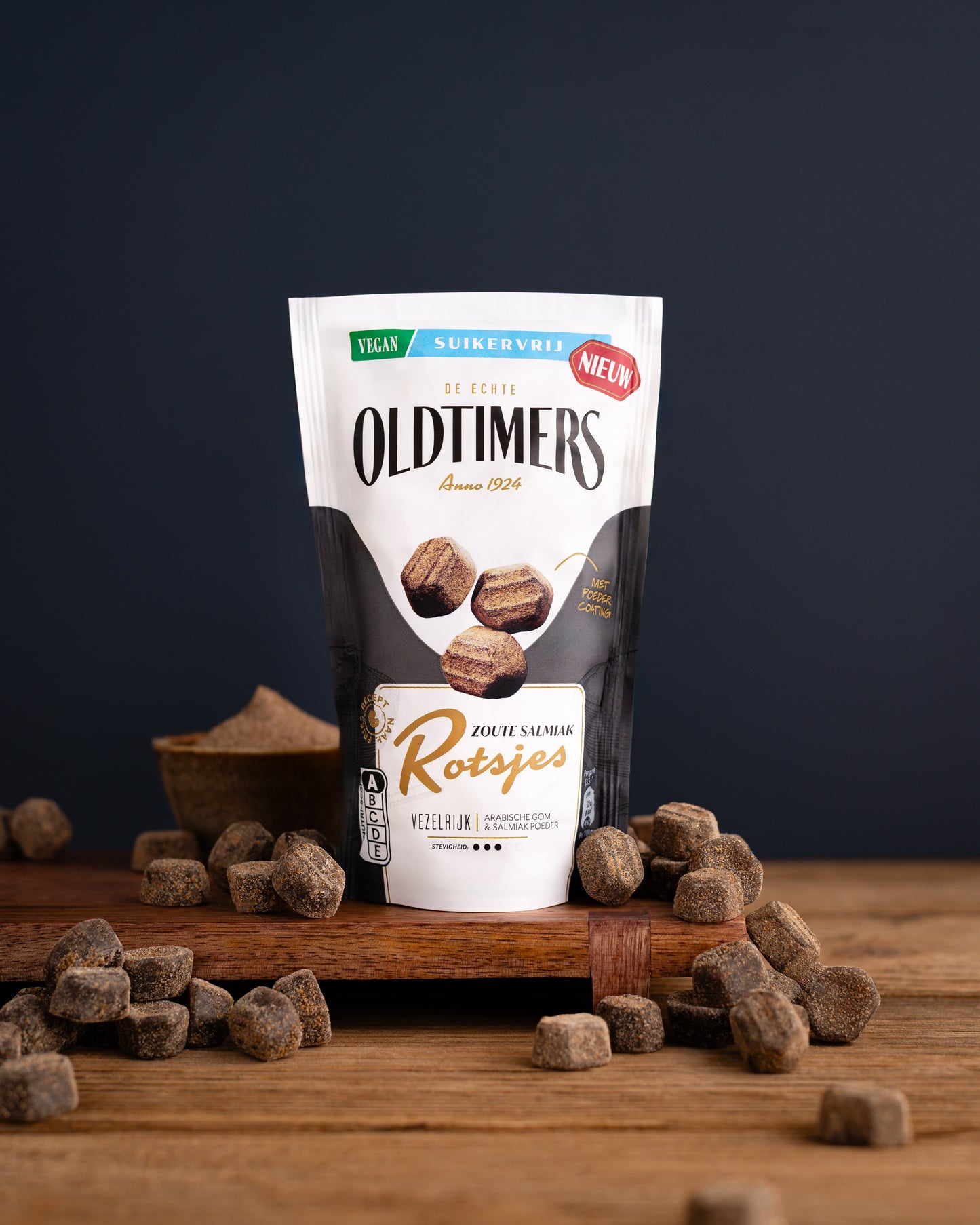 Zak Oldtimers Zoute Salmiak Rotsjes suikervrij snoep met losse salmiakrotsjes op een houten ondergrond. Vegan drop met zout- en salmiaksmaak.