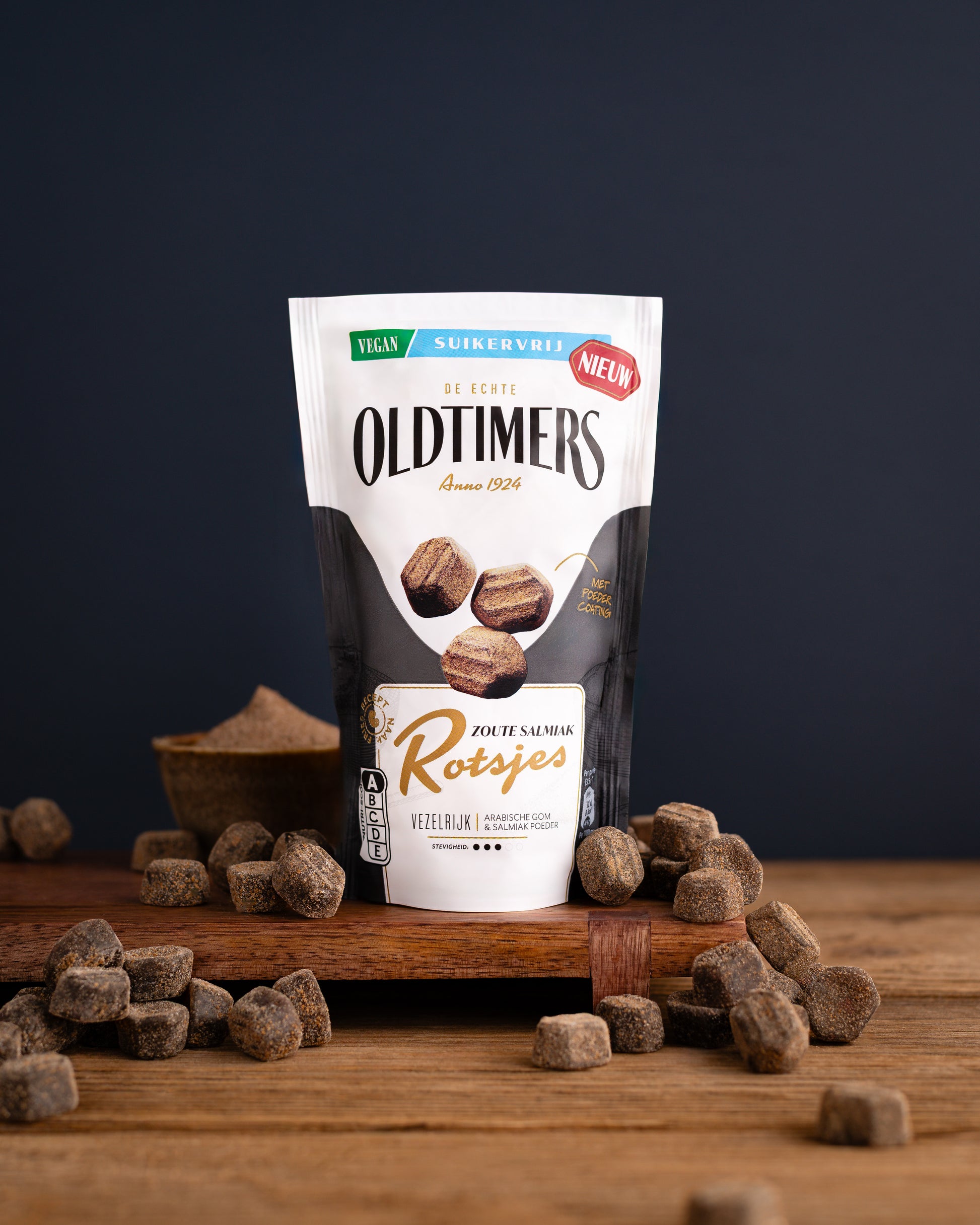 Zak Oldtimers Zoute Salmiak Rotsjes suikervrij snoep met losse salmiakrotsjes op een houten ondergrond. Vegan drop met zout- en salmiaksmaak.